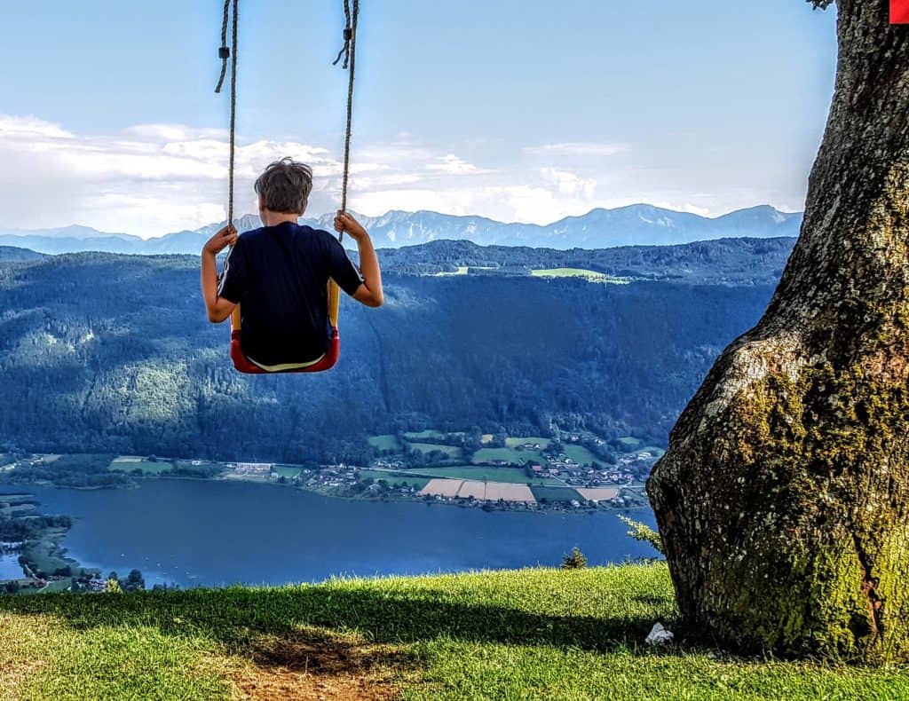 Kind auf Schaukel am Ossiachberg mit Blick auf Ossiacher See und Bleistätter Moor