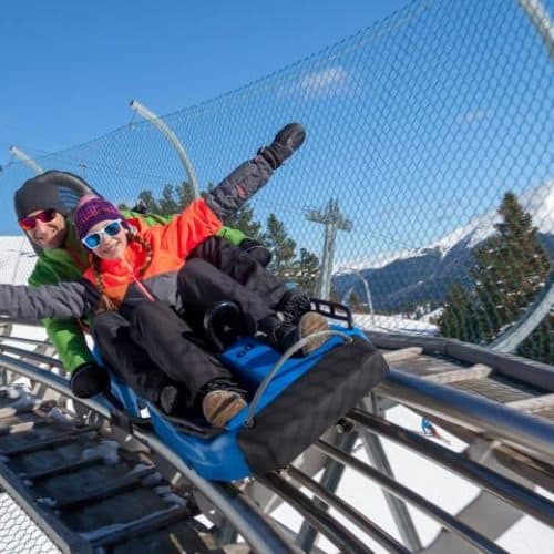 Nocky Flitzer Turracher Höhe Rodelbahn TOP 10 Ausflugsziele Kärnten Steiermark im Winter. Vater mit Kind beim Rodeln.