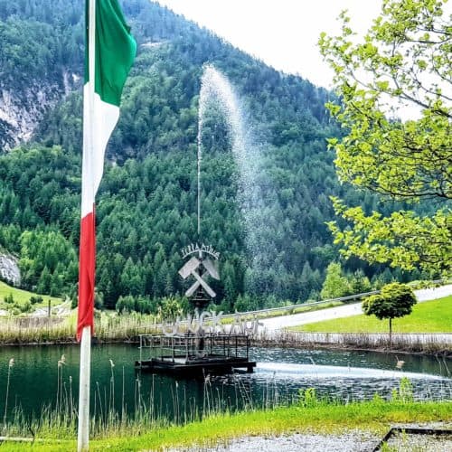 Teich mit Brunnen und Fahnen vor Schaubergwerk Terra Mystica im Naturpark Dobratsch